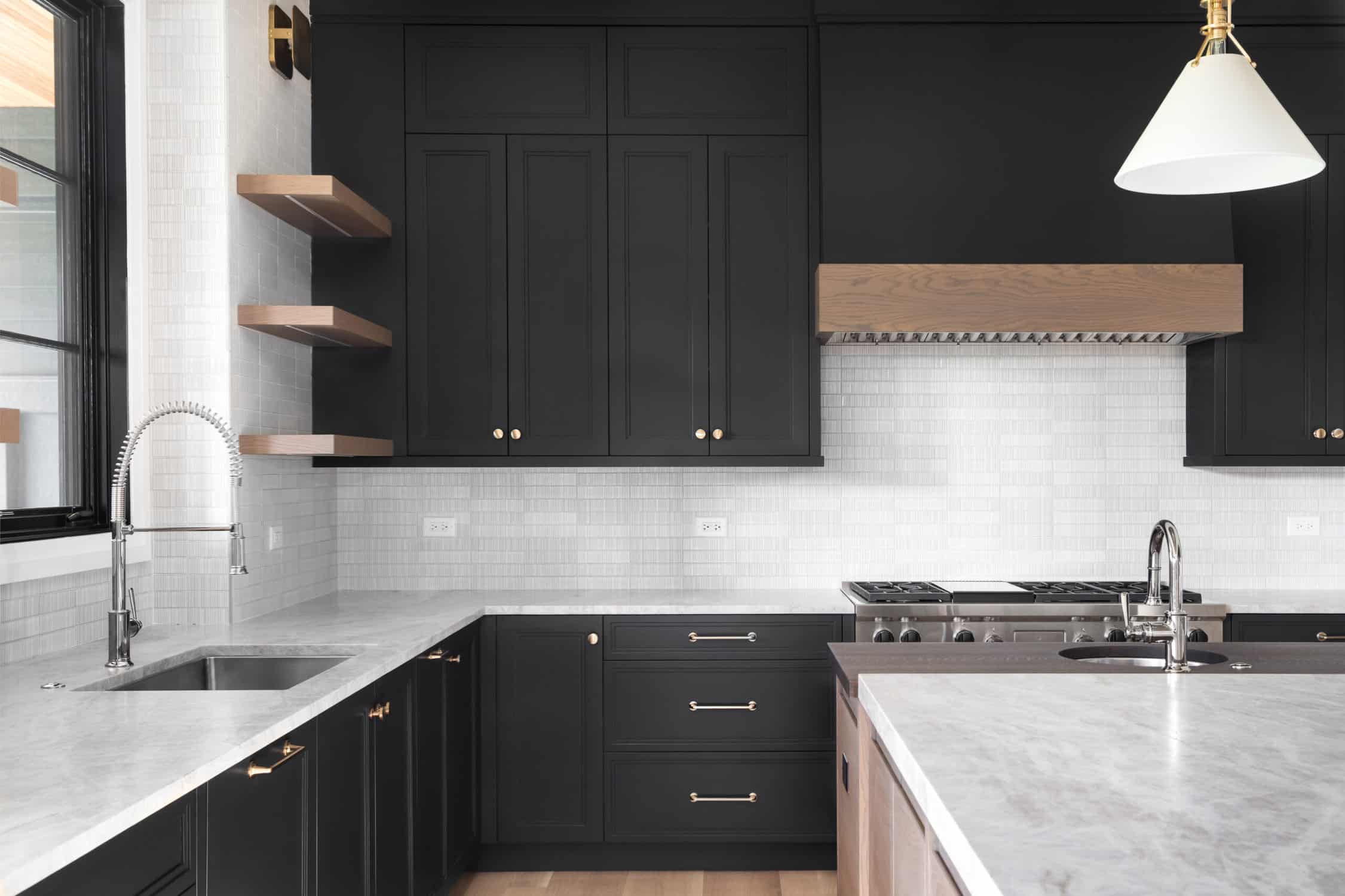 A luxury kitchen with black cabinets, granite counter top, tiled backsplash, stainless steel appliances, and chrome faucets.