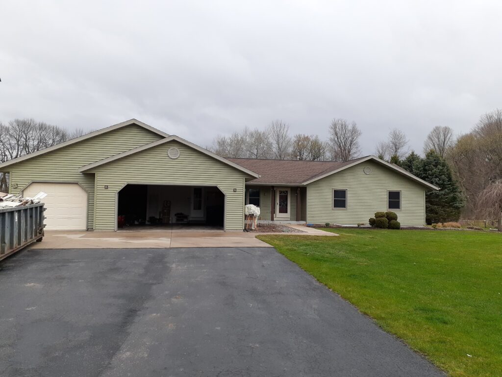 Green house with large garage and stone driveway