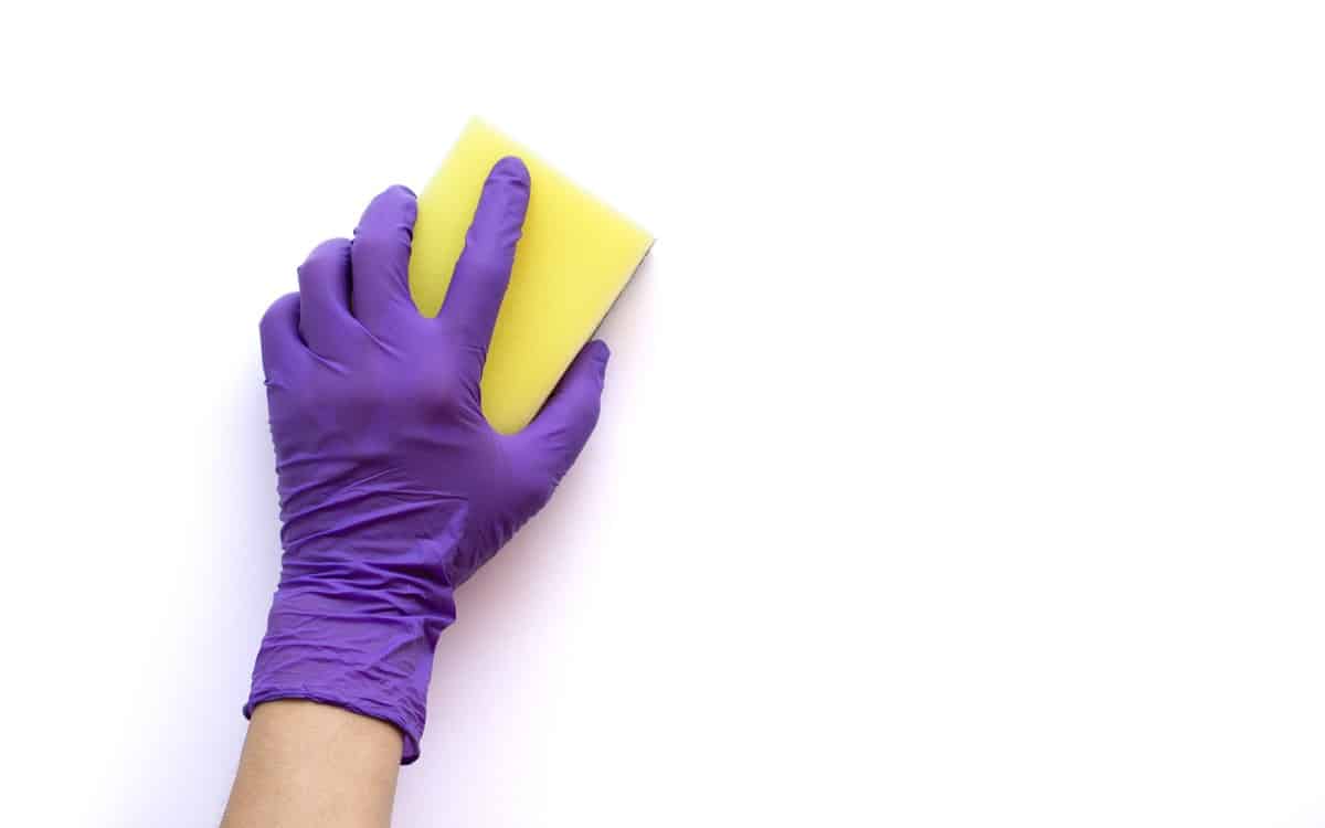 a woman's gloved hand with sponge, cleaning a white wall