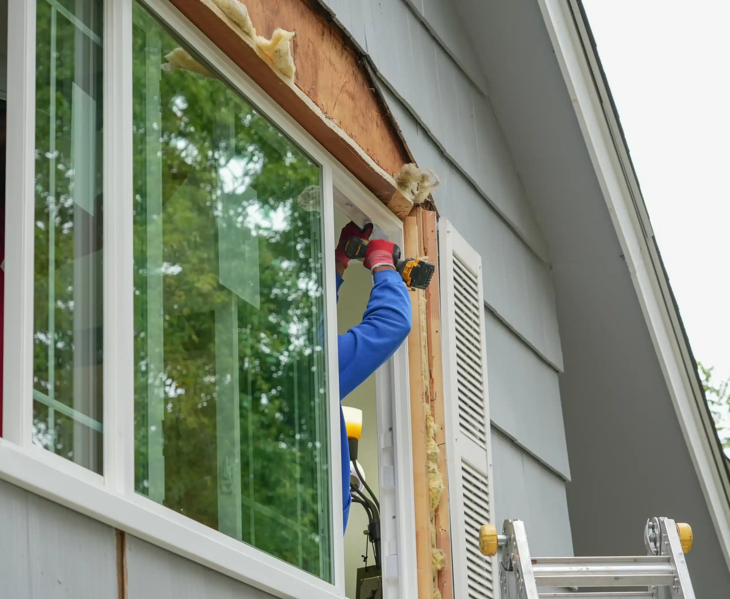 Professional Window Installation for Home Exterior Renovation A professional contractor installing a new white window frame on a house during exterior renovation.