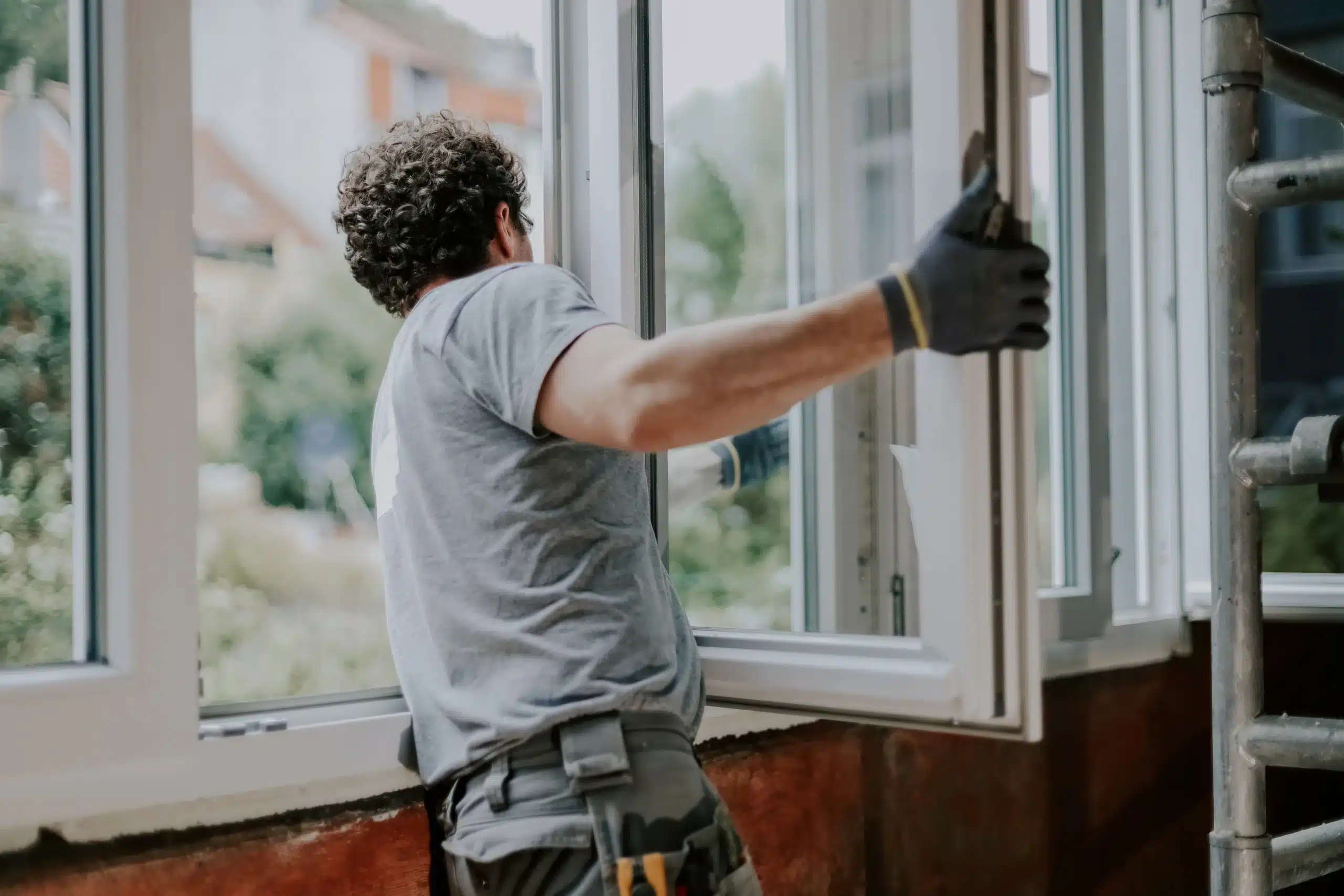Interior Window Installation for Home Remodel and Renovation A worker installing a new white window frame inside a home undergoing a renovation project.