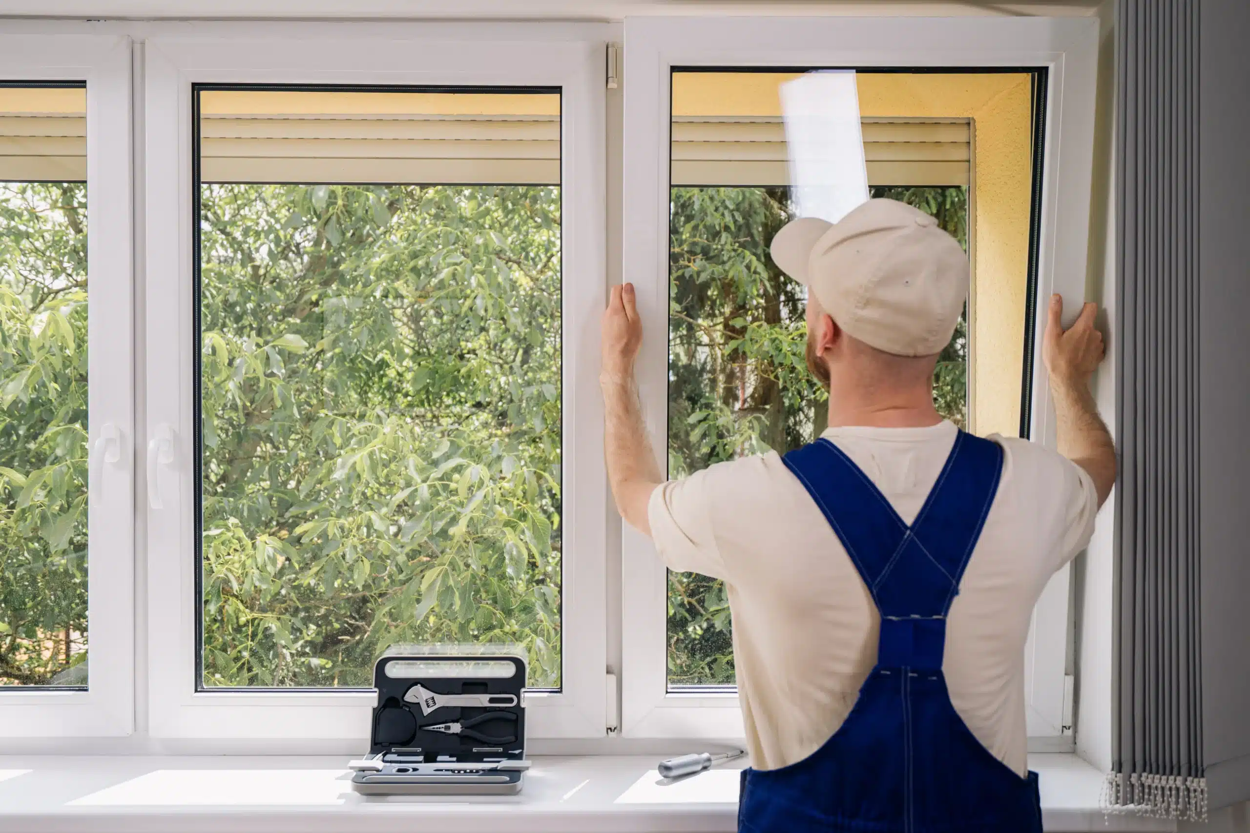 Professional Window Installation Service Professional installer fitting a white modern window inside a home with trees visible outside and tools on the windowsill