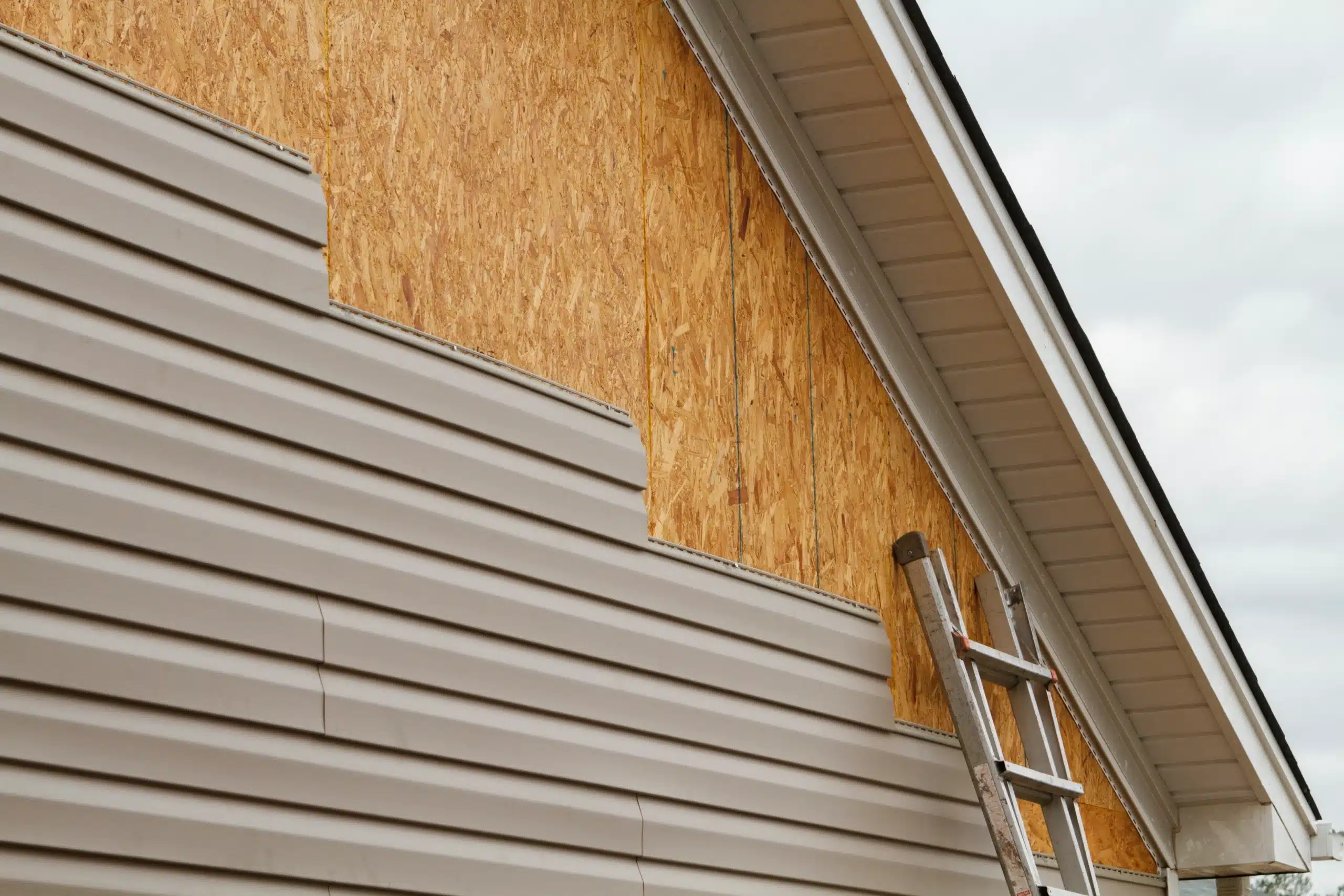 Exterior Siding Replacement for Home Renovation Projects House exterior with partially installed light brown vinyl siding, revealing wood sheathing and a ladder.