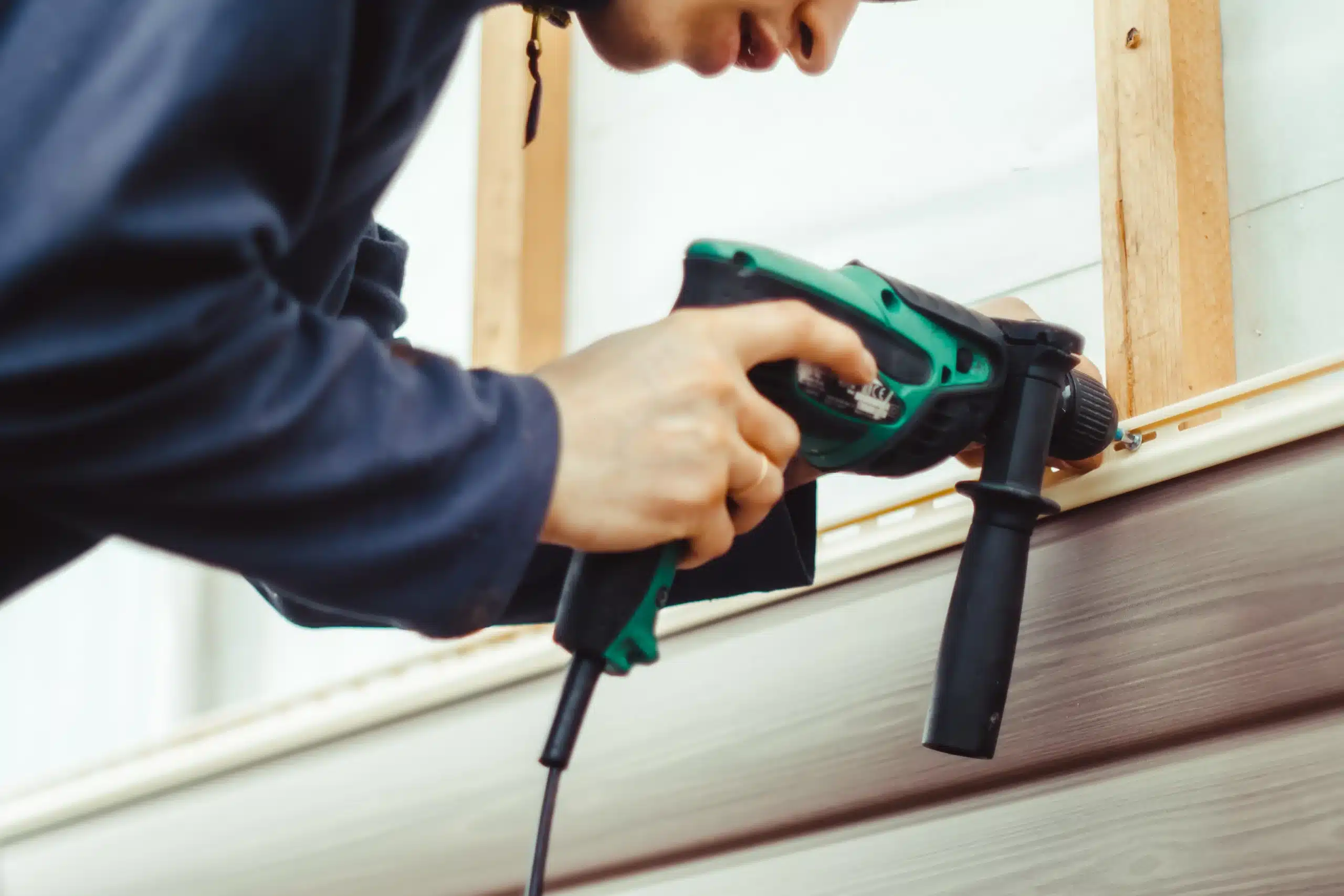 Professional exterior siding installation and repair A professional contractor installs new exterior siding panels on a home using a power drill.