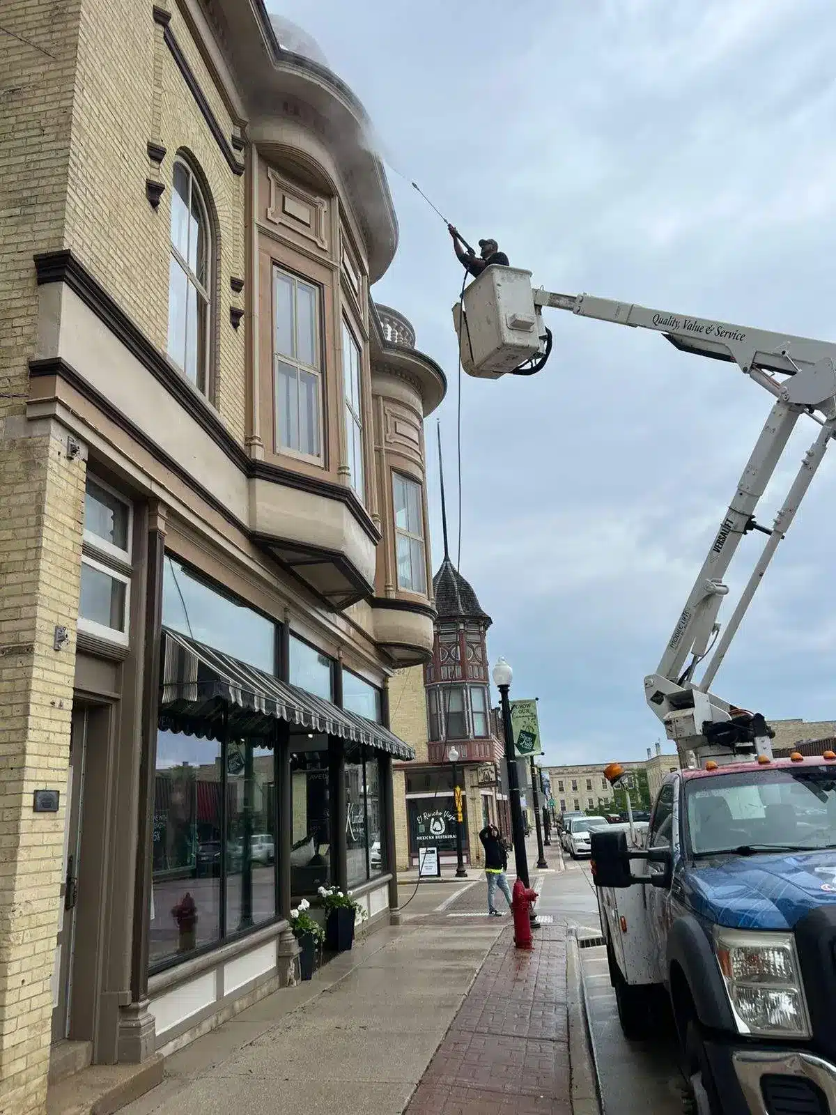 Commercial Building Pressure Washing and Exterior Cleaning A worker in a cherry picker pressure washing the brick exterior of a commercial building on a city street.