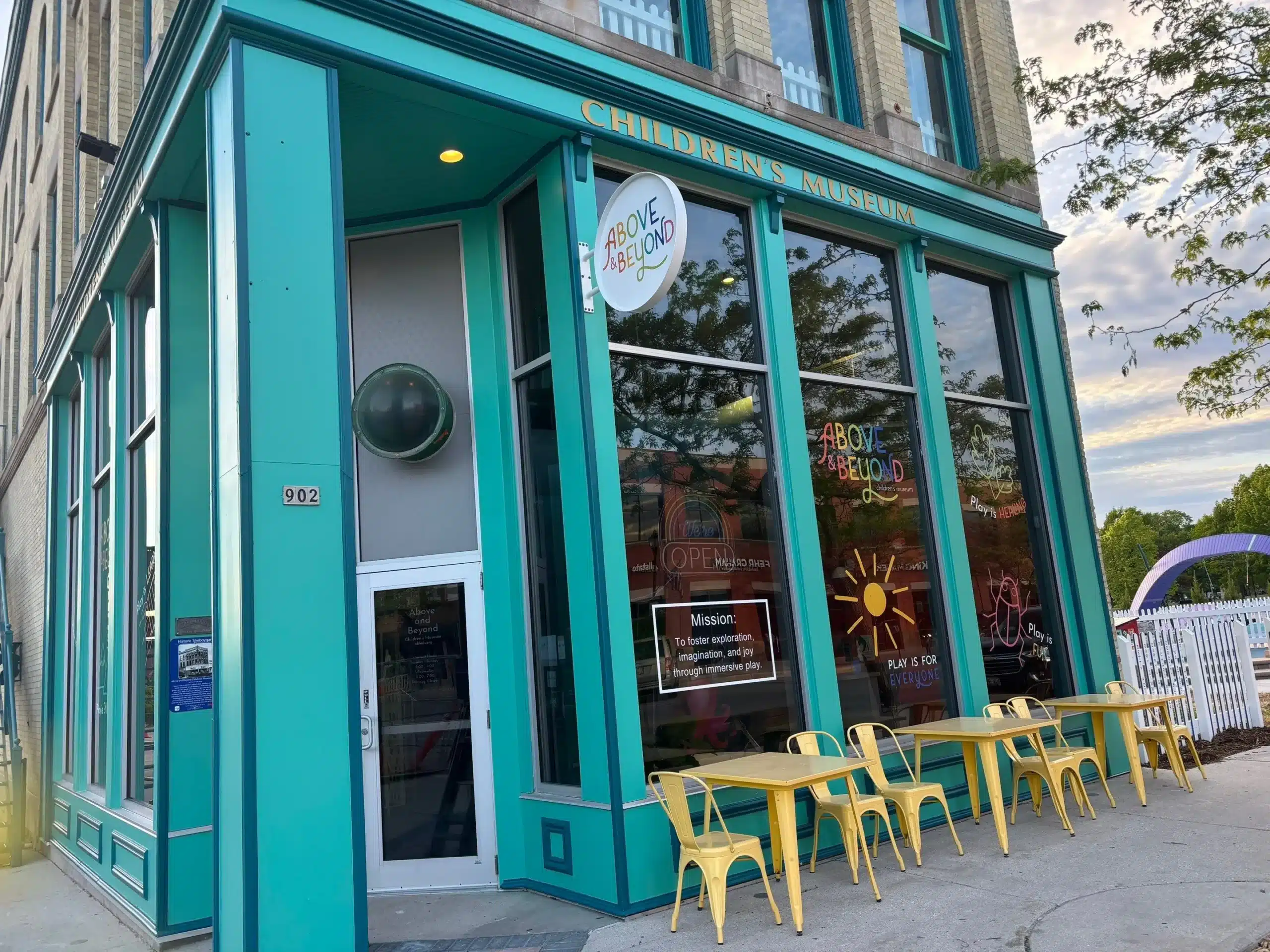 Vibrant Commercial Storefront and Museum Exterior Painting Bright teal commercial building, a children's museum, with large windows and yellow outdoor seating.
