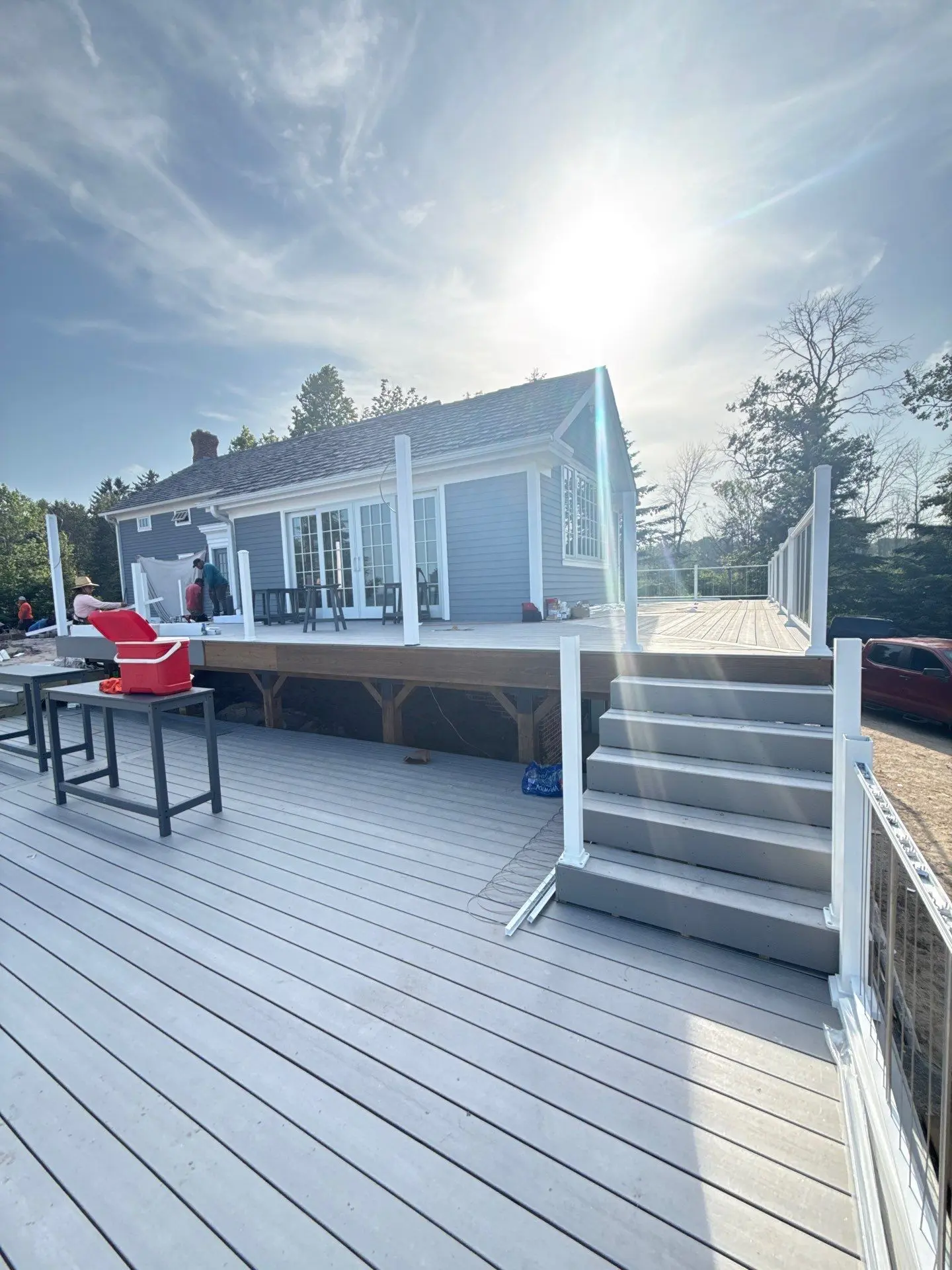 Expert Exterior House and Deck Painting Services A beautiful light blue house with a newly painted multi level gray deck and white railings under a bright sky.