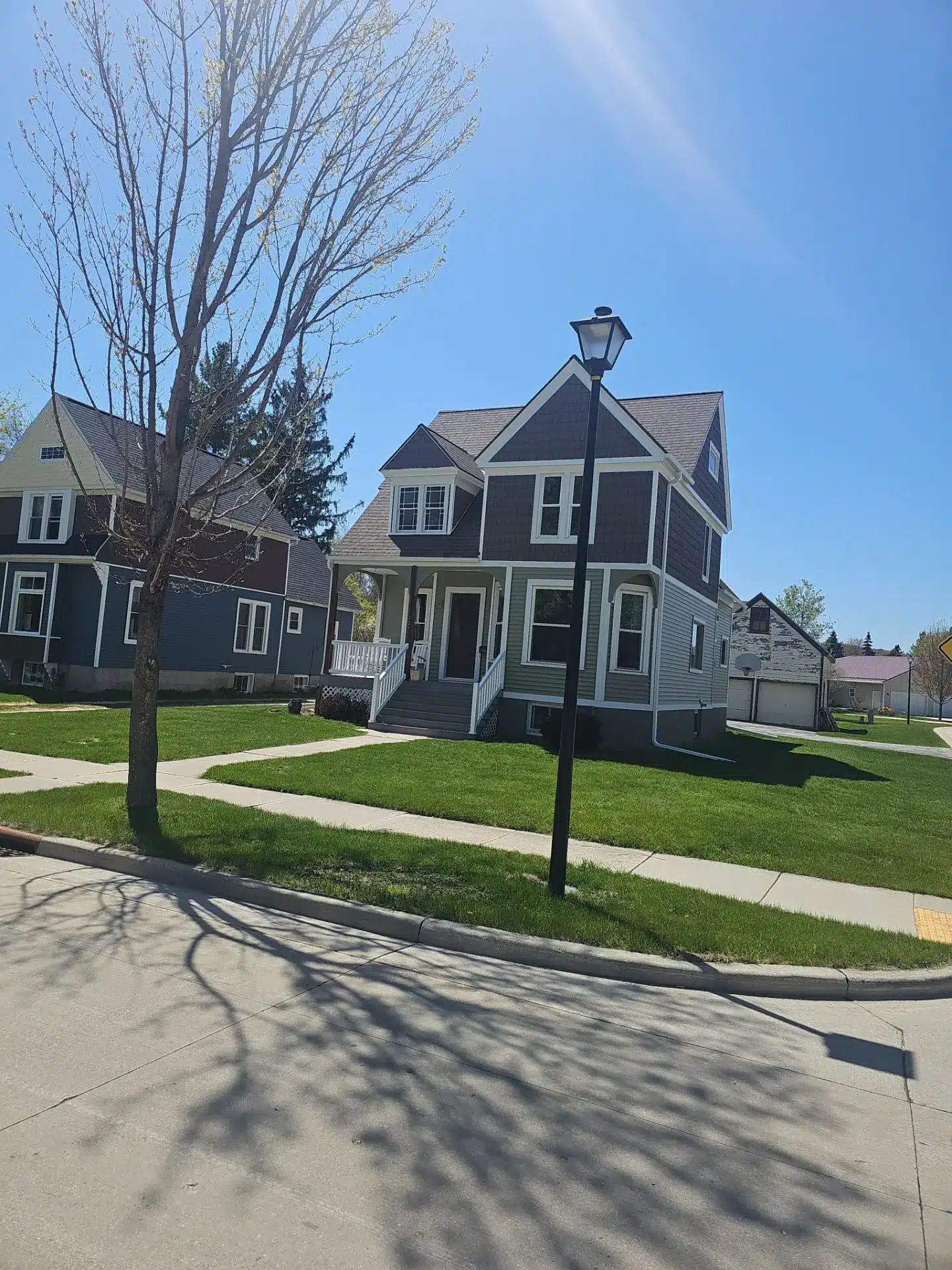 Residential Exterior House Painting and Siding Refresh A charming two story house with light green and gray siding, white trim, and a welcoming front porch.