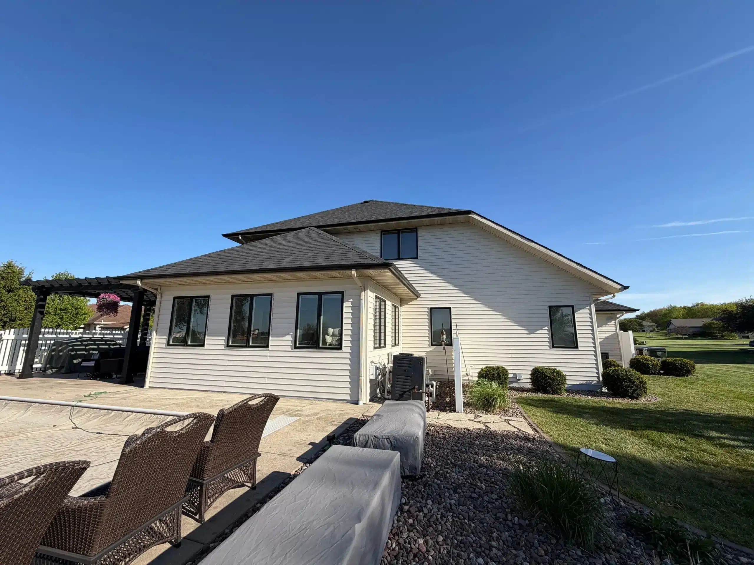 Modern White Exterior House Painting with Black Trim The rear view of a large white house with black window frames, a dark roof, and a patio area.