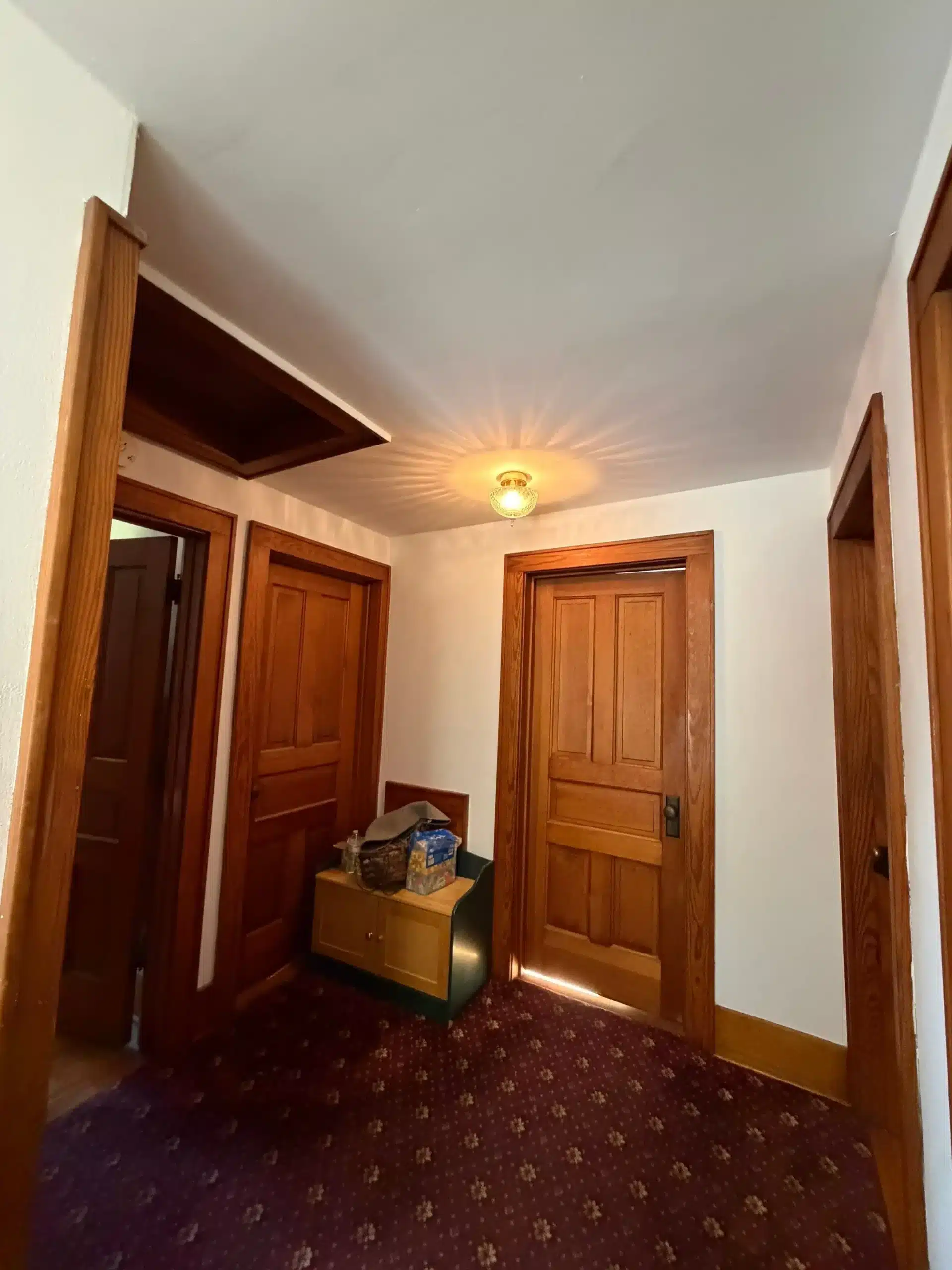 Professional Interior Hallway and Trim Painting A cozy interior hallway with freshly painted white walls, warm wooden doors, trim, and a patterned carpet.