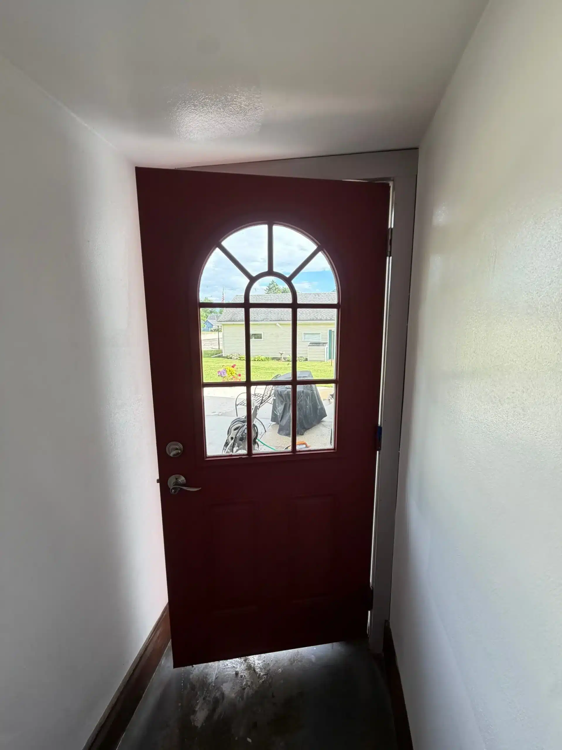 Expert Interior and Exterior Door Painting Services A freshly painted reddish brown arched door with glass panes, viewed from inside a white walled entryway.
