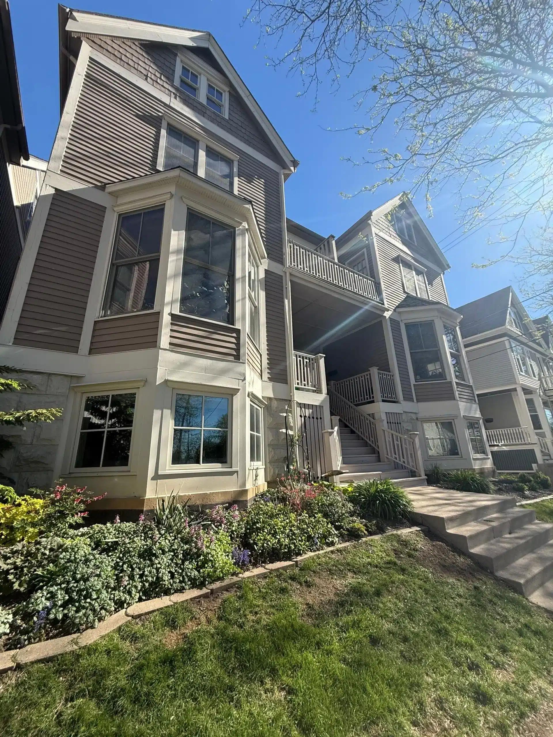 Multi Unit Residential Exterior Painting and Building Refresh A multi story residential building with brown siding, white trim, bay windows, and balconies, surrounded by landscaping.